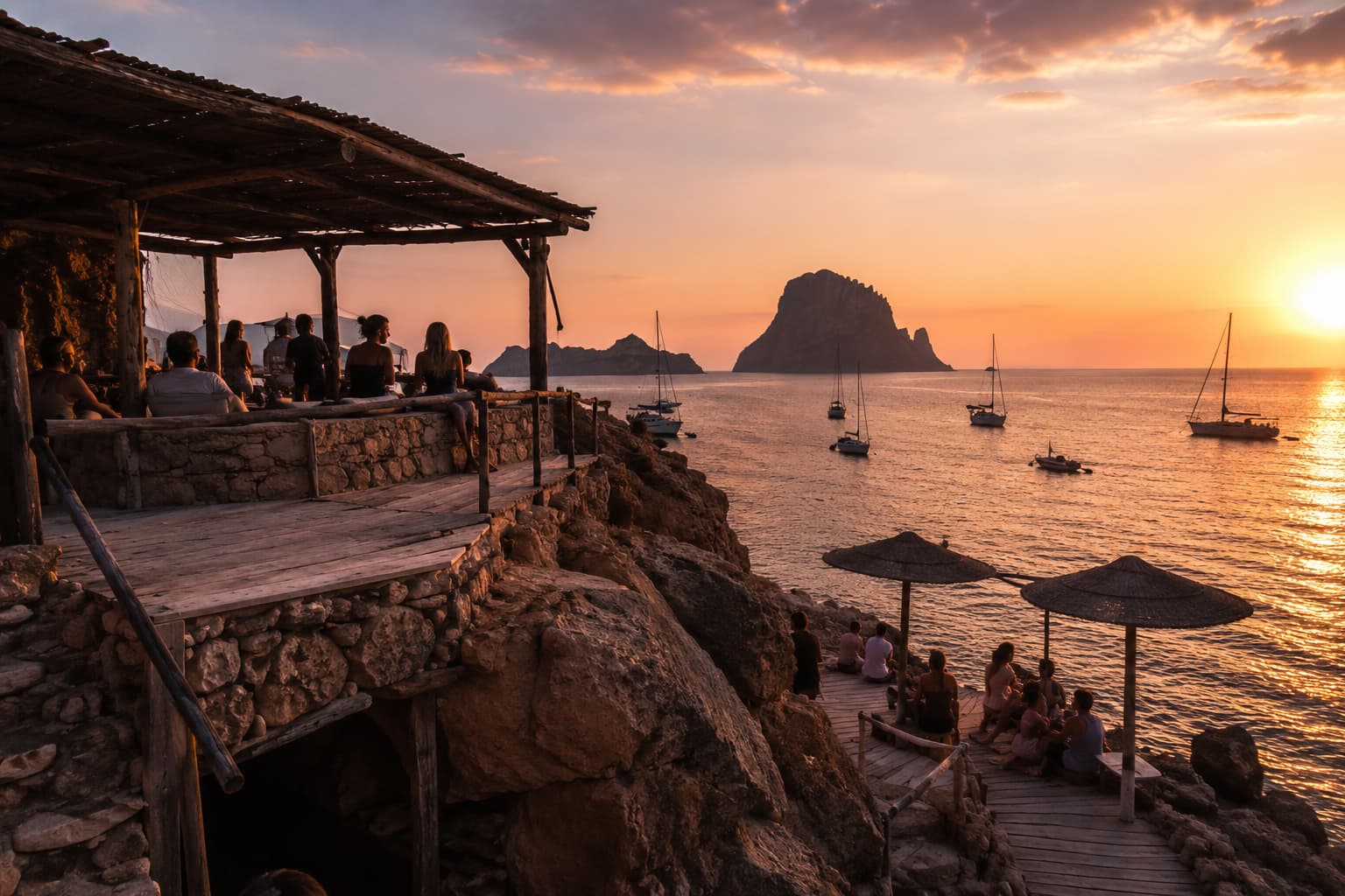 Terraza del chiringuito sobre las rocas, minutos antes del último sol, con veleros fondeados